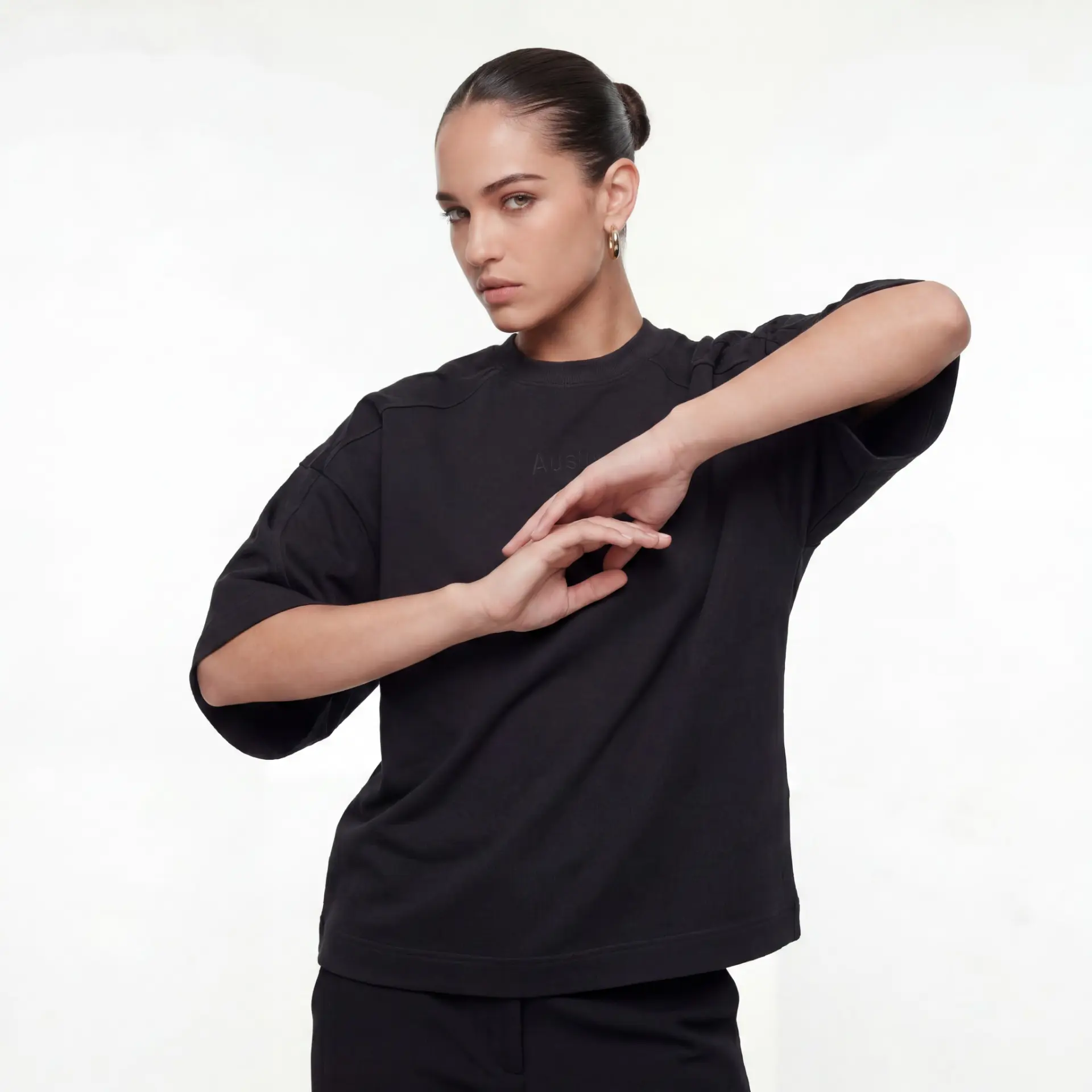AUSLUB model pose — woman in black oversized tee and trousers against a neutral backdrop