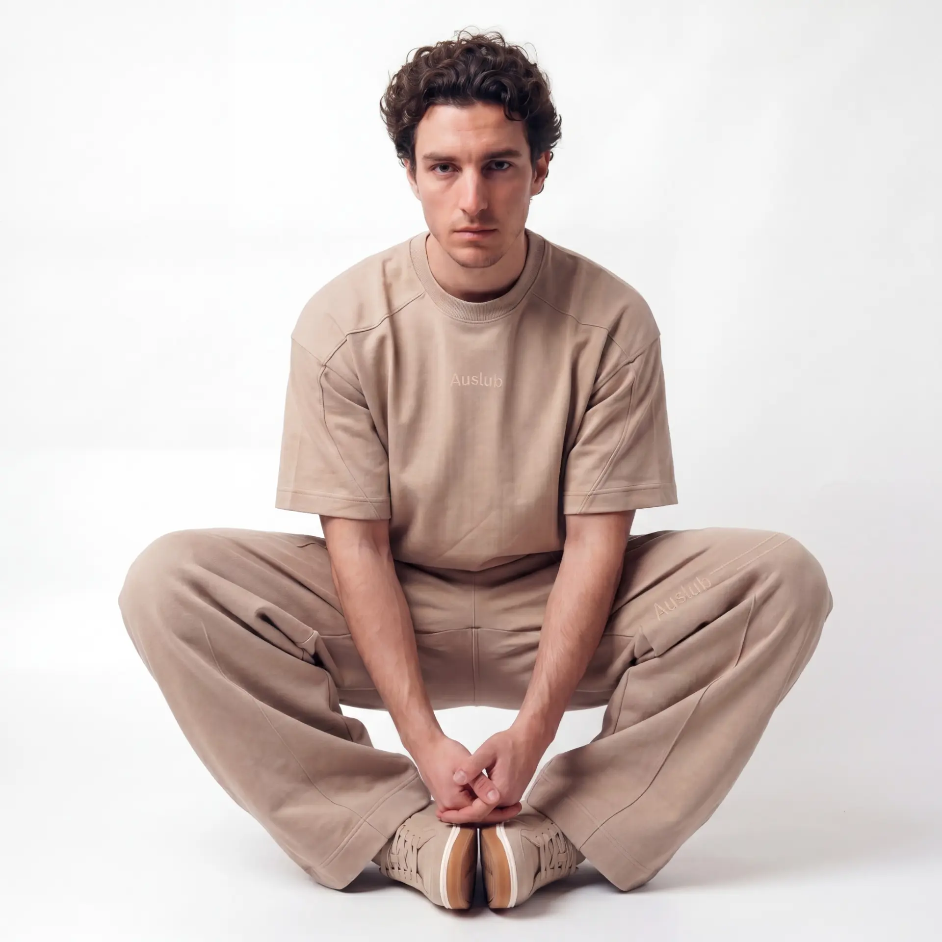 AUSLUB model sitting — man in tonal beige cropped tee and trousers with Auslub embroidery