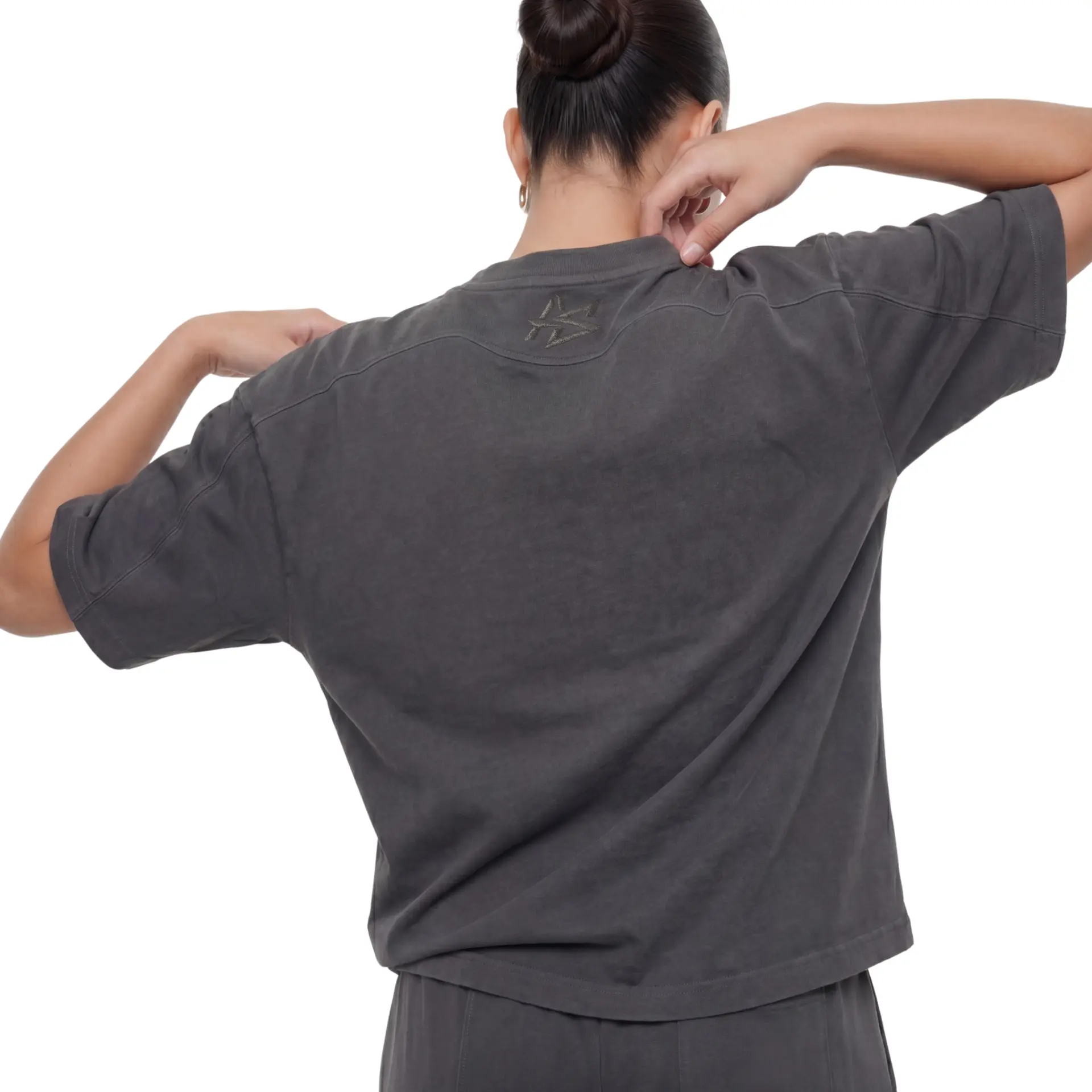 AUSLUB studio portrait — back view of a woman in a charcoal oversized tee with tonal embroidery