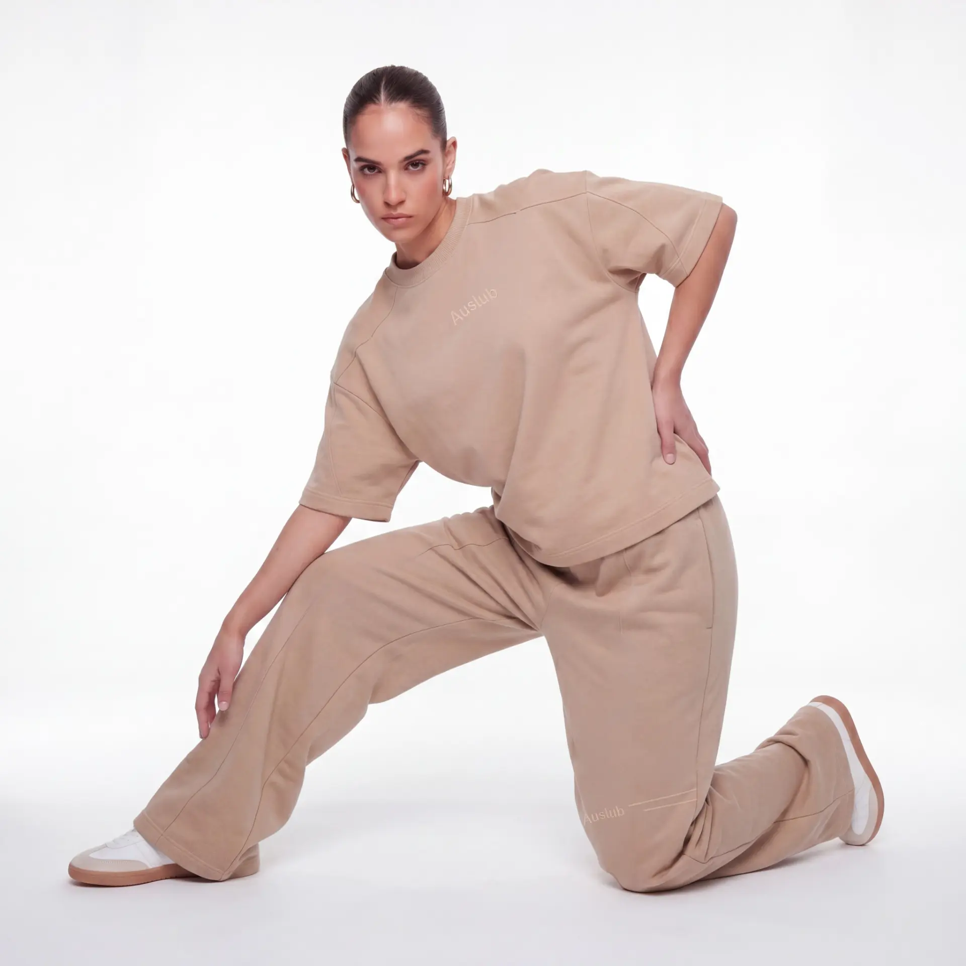 AUSLUB model kneeling — woman in tonal beige cropped tee and matching trousers with Auslub embroidery